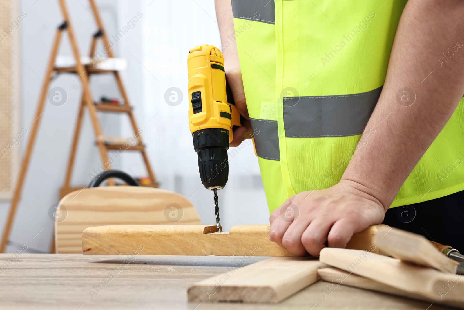 Photo of Young worker using electric drill at table in workshop, closeup