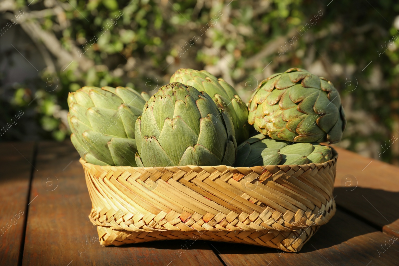 Photo of Tasty fresh raw artichokes on wooden table outdoors, closeup