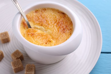 Delicious creme brulee in bowl served on light blue wooden table, closeup