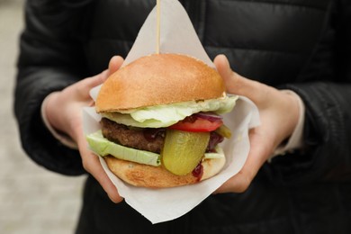 Woman holding fresh delicious burger outdoors, closeup. Street food