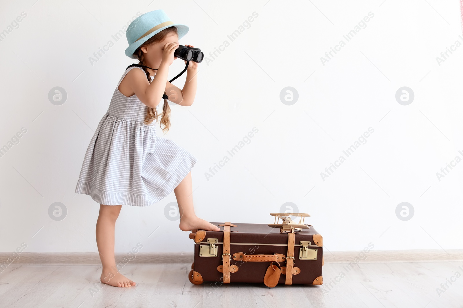 Photo of Adorable little child playing traveler with suitcase indoors