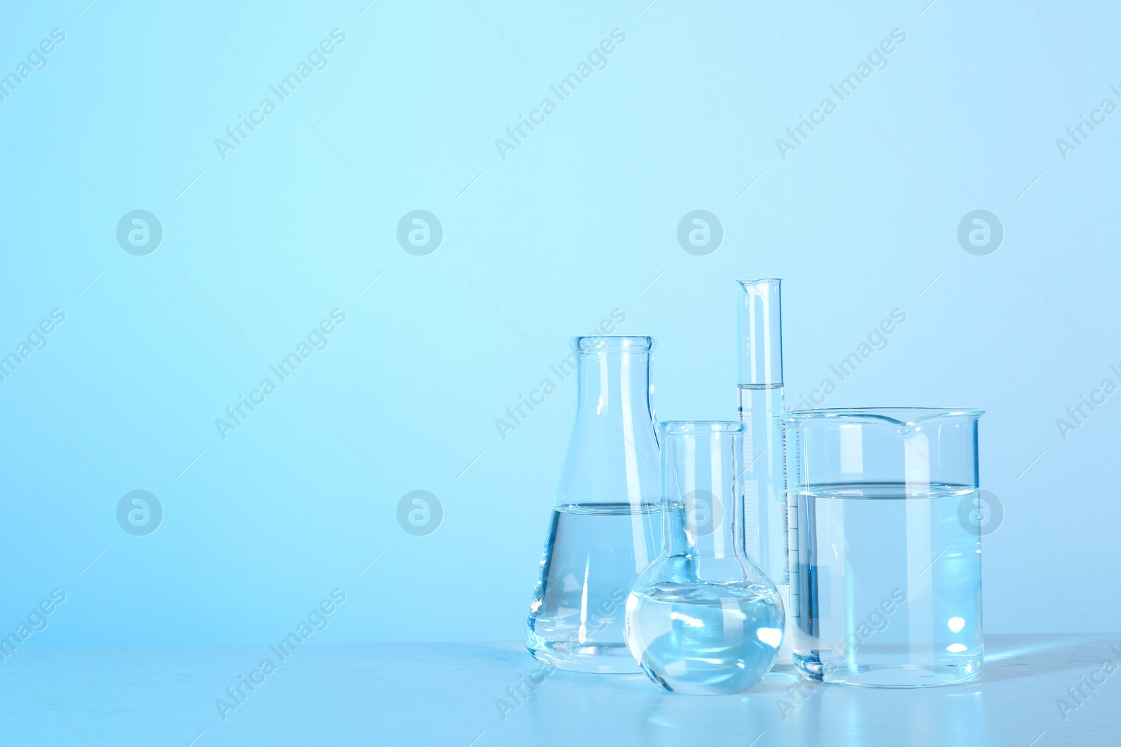 Photo of Laboratory glassware with liquid on table against color background. Chemical analysis