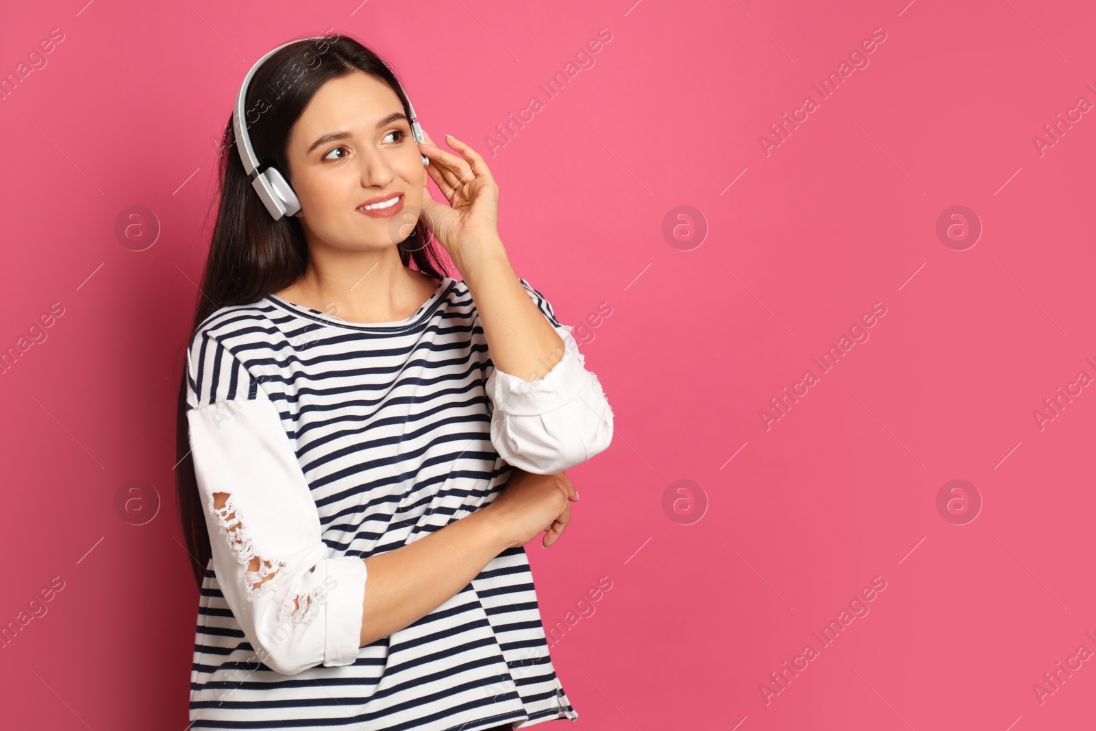 Photo of Young woman listening to audiobook on pink background. Space for text