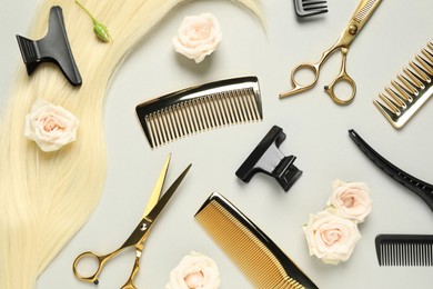 Photo of Flat lay composition with professional hairdresser tools, flowers and blonde hair strand on light grey background
