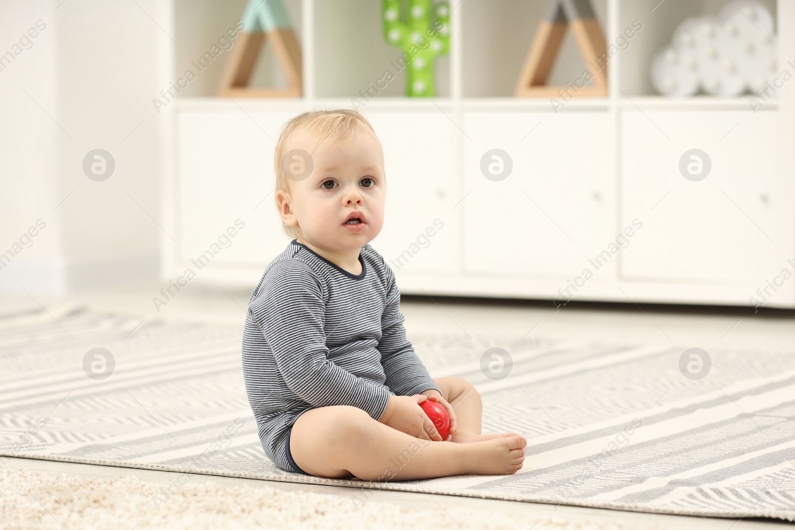 Photo of Children toys. Cute little boy with colorful red ball on rug at home