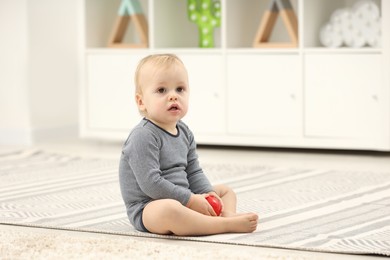 Children toys. Cute little boy with colorful red ball on rug at home