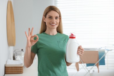 Photo of Woman holding fabric softener and showing OK gesture in bathroom