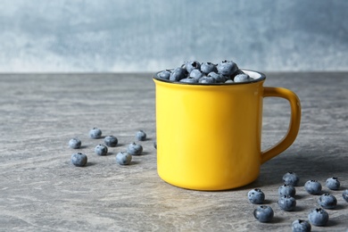 Photo of Fresh blueberries in yellow cup on color table. Space for text