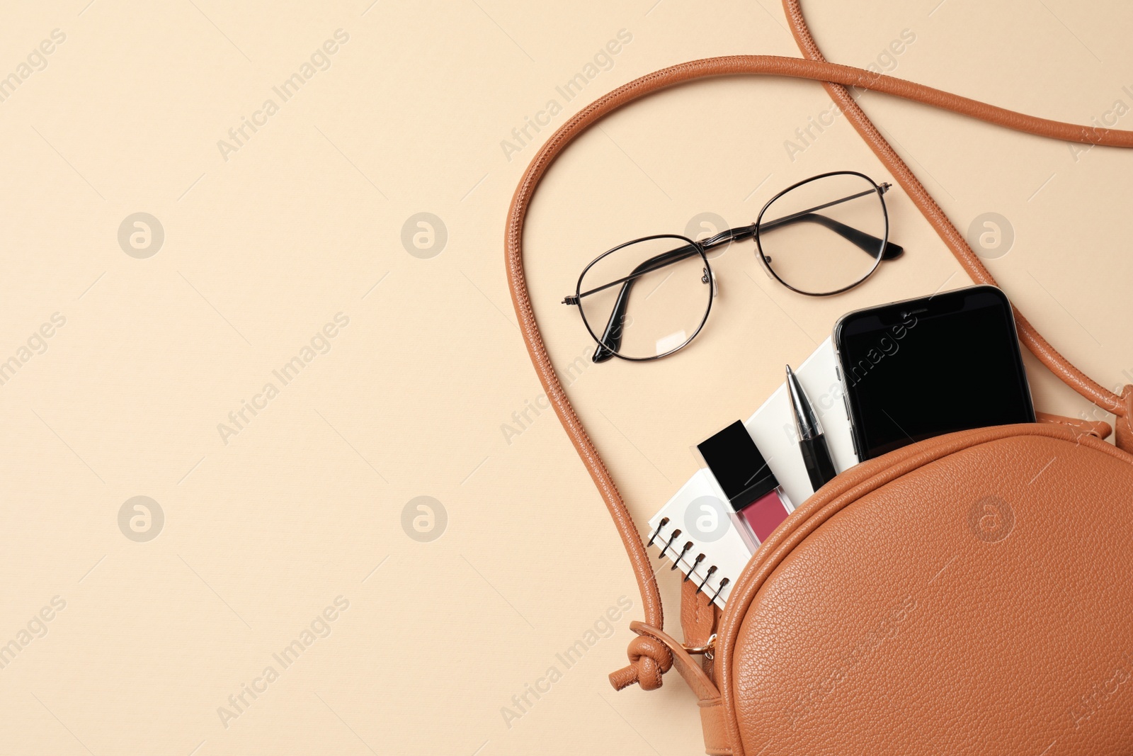 Photo of Stylish woman's bag with smartphone and accessories on beige background, flat lay. Space for text