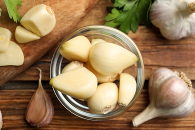 Photo of Fresh peeled garlic cloves in bowl and bulbs on wooden table, flat lay. Organic product