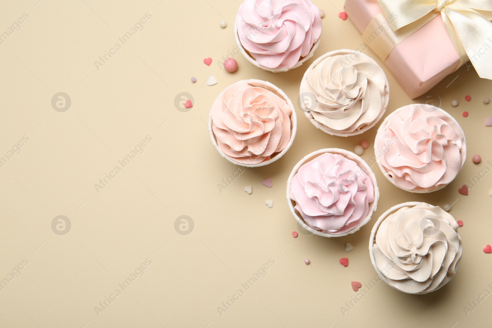 Photo of Delicious birthday cupcakes, gift box and sprinkles on beige background, flat lay. Space for text