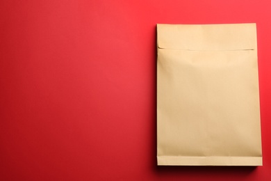 Photo of Kraft paper envelope on red background, top view. Space for text