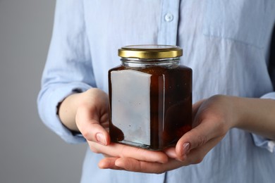 Woman holding jar of tasty sweet fig jam on grey background, closeup