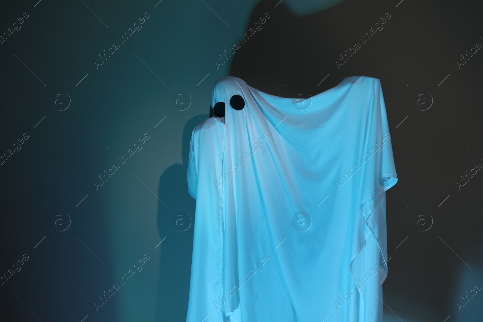 Photo of Creepy ghost. Woman covered with sheet in color light