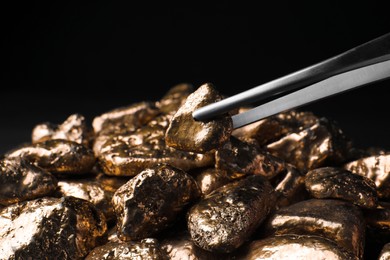 Photo of Tweezers with gold nugget above pile against black background, closeup