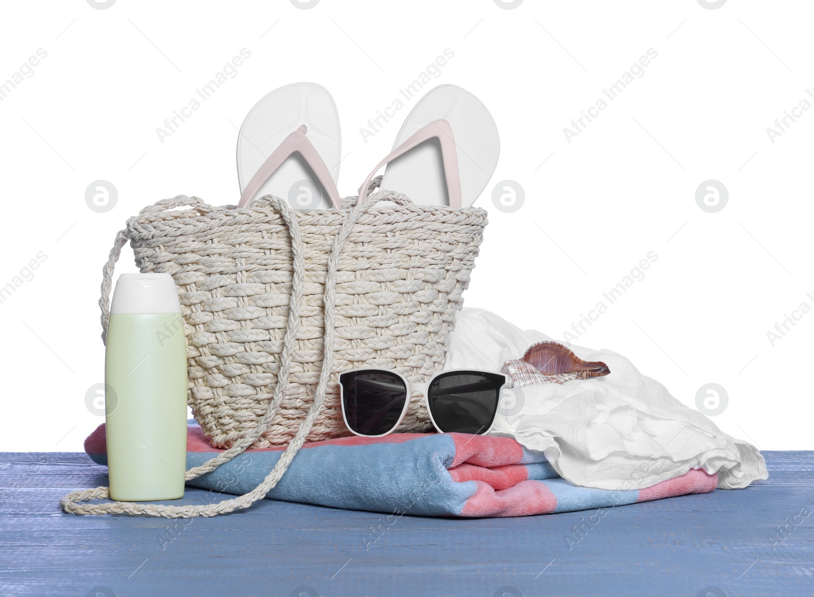 Photo of Stylish bag, sunscreen and other beach accessories on grey wooden table against white background