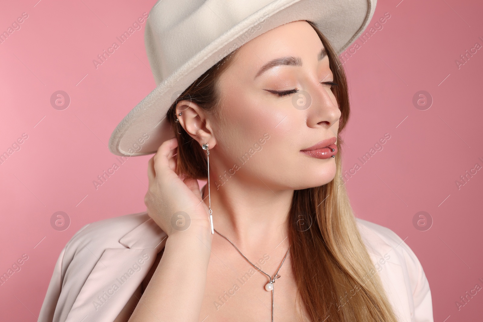 Photo of Young woman with lip and ear piercings on pink background