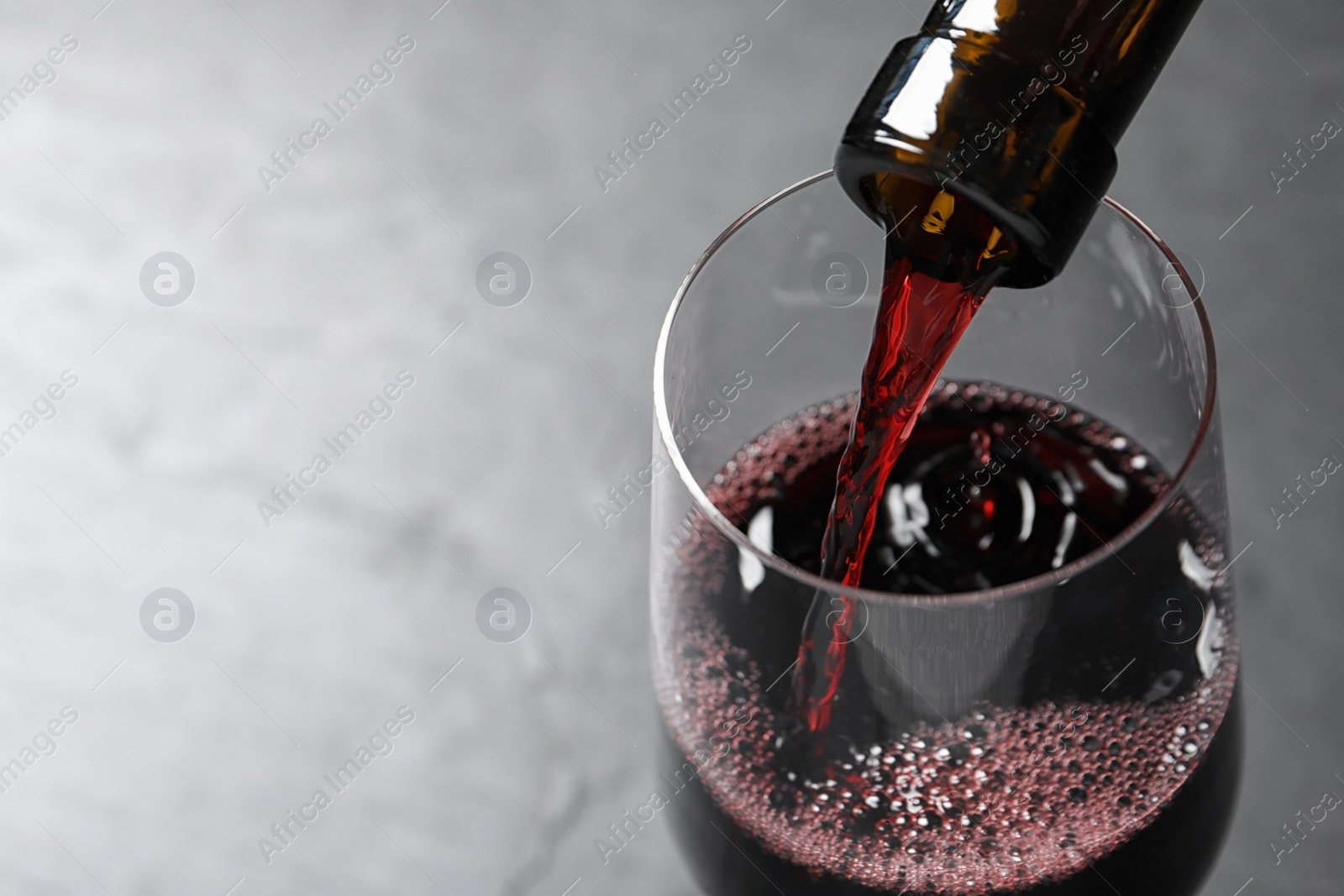 Photo of Pouring red wine from bottle into glass on grey background, closeup. Space for text