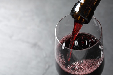 Pouring red wine from bottle into glass on grey background, closeup. Space for text