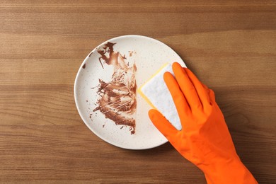 Photo of Woman washing dirty plate at wooden table, top view