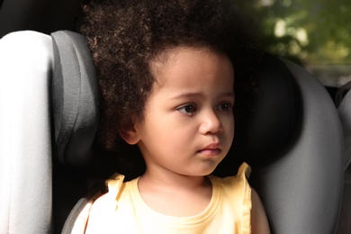 Photo of Little African-American girl crying alone inside car. Child in danger