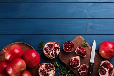 Photo of Delicious ripe pomegranates on blue wooden table, flat lay. Space for text