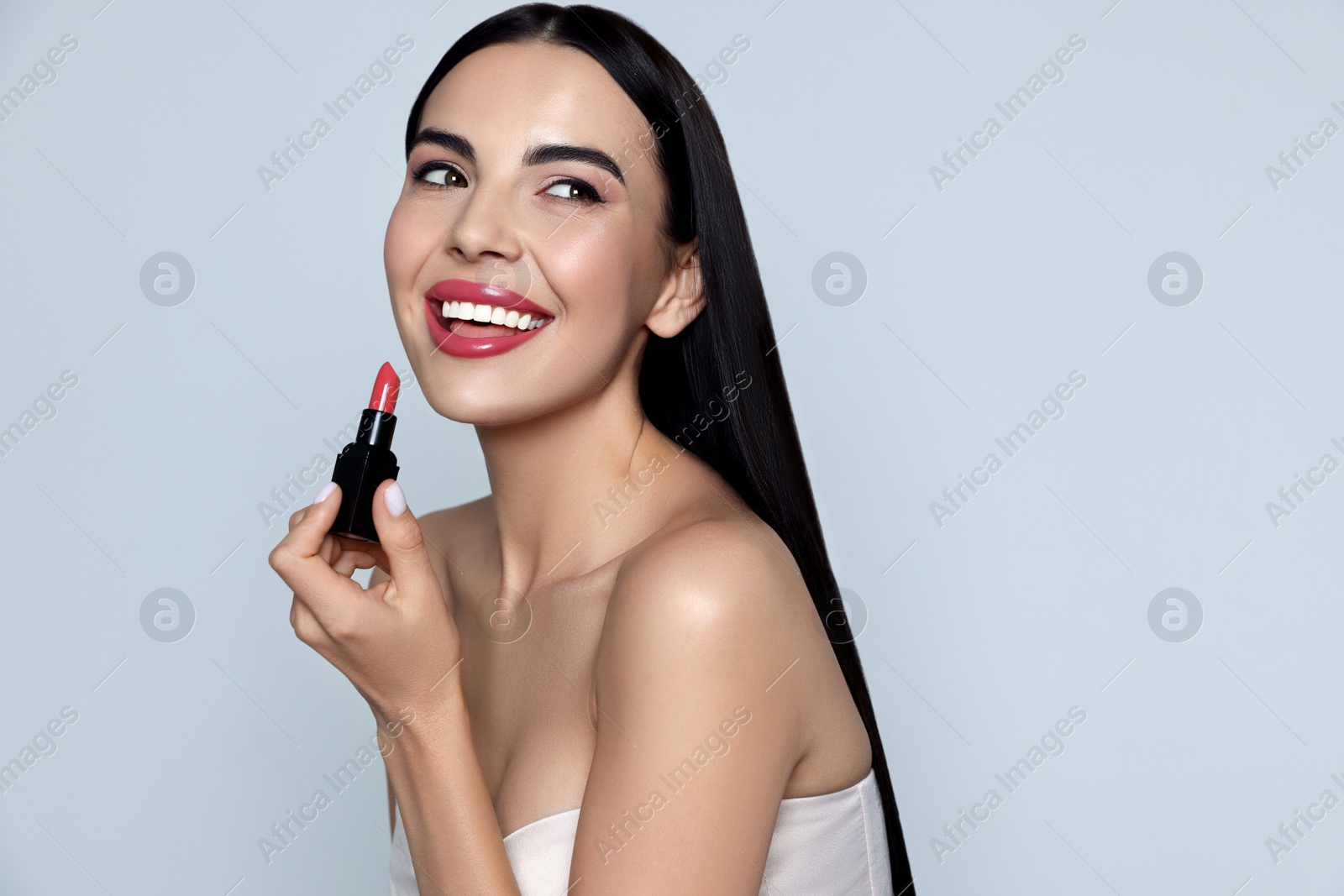 Image of Young woman with beautiful makeup holding glossy lipstick on light gray background