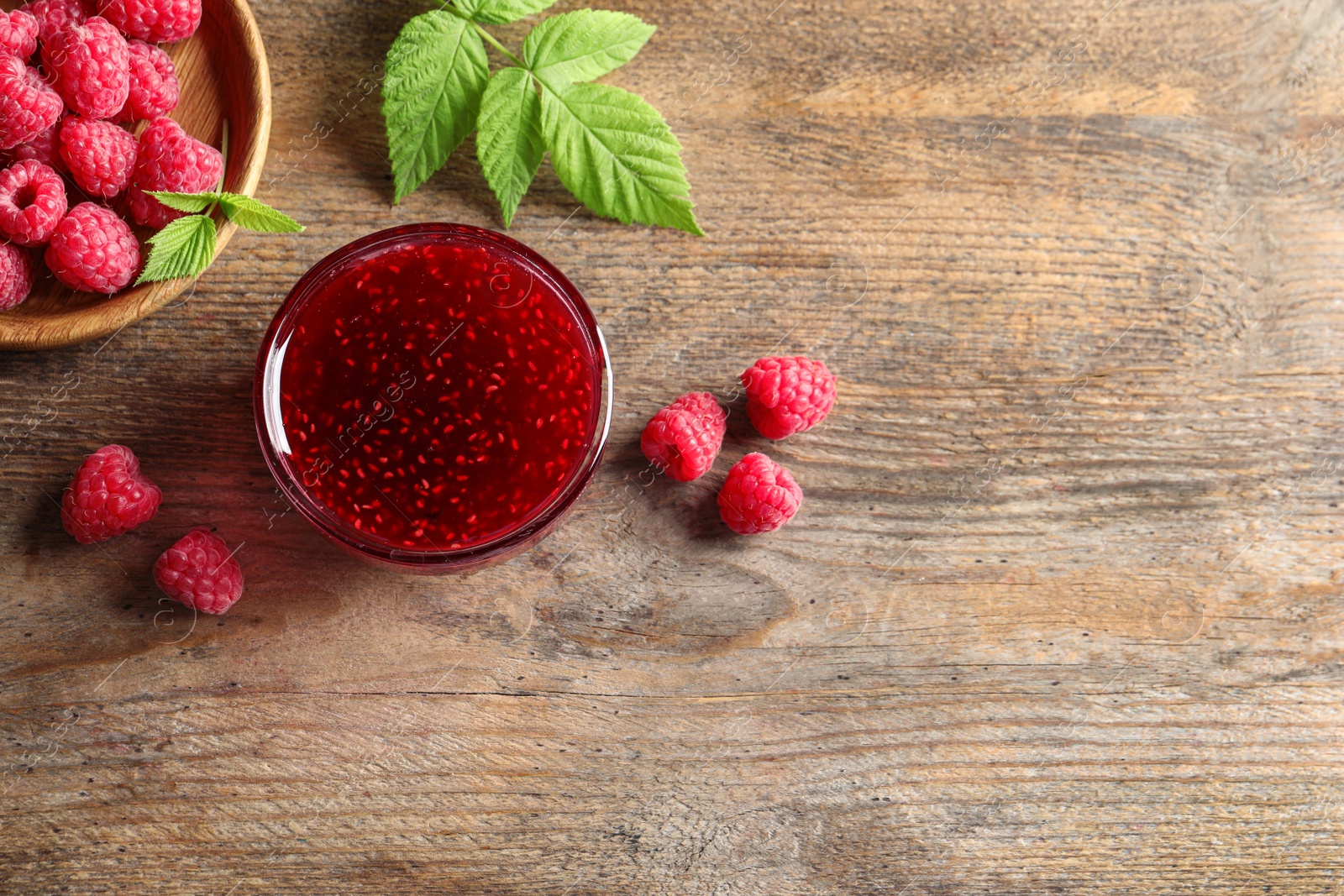 Image of Sweet raspberry jam and fresh berries on wooden table, flat lay. Space for text