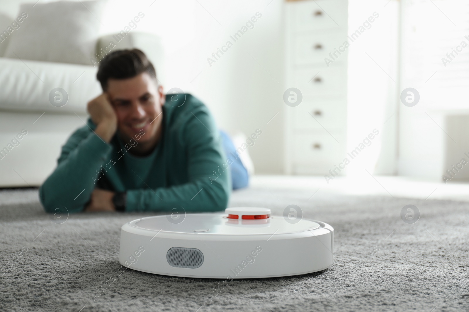 Photo of Man resting while robotic vacuum cleaner doing his work at home
