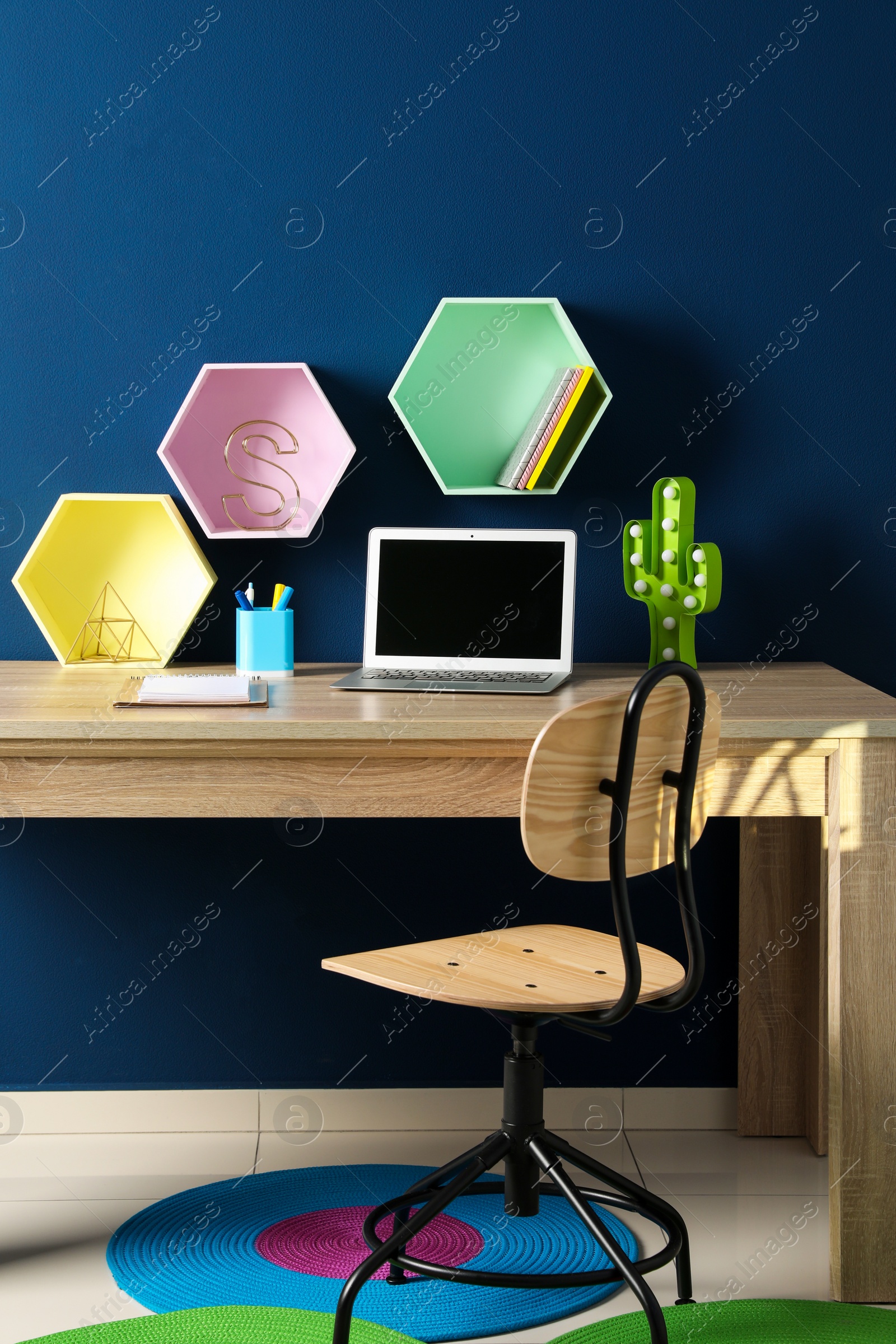 Photo of Comfortable workplace with modern laptop and stationery near blue wall in child room. Interior design