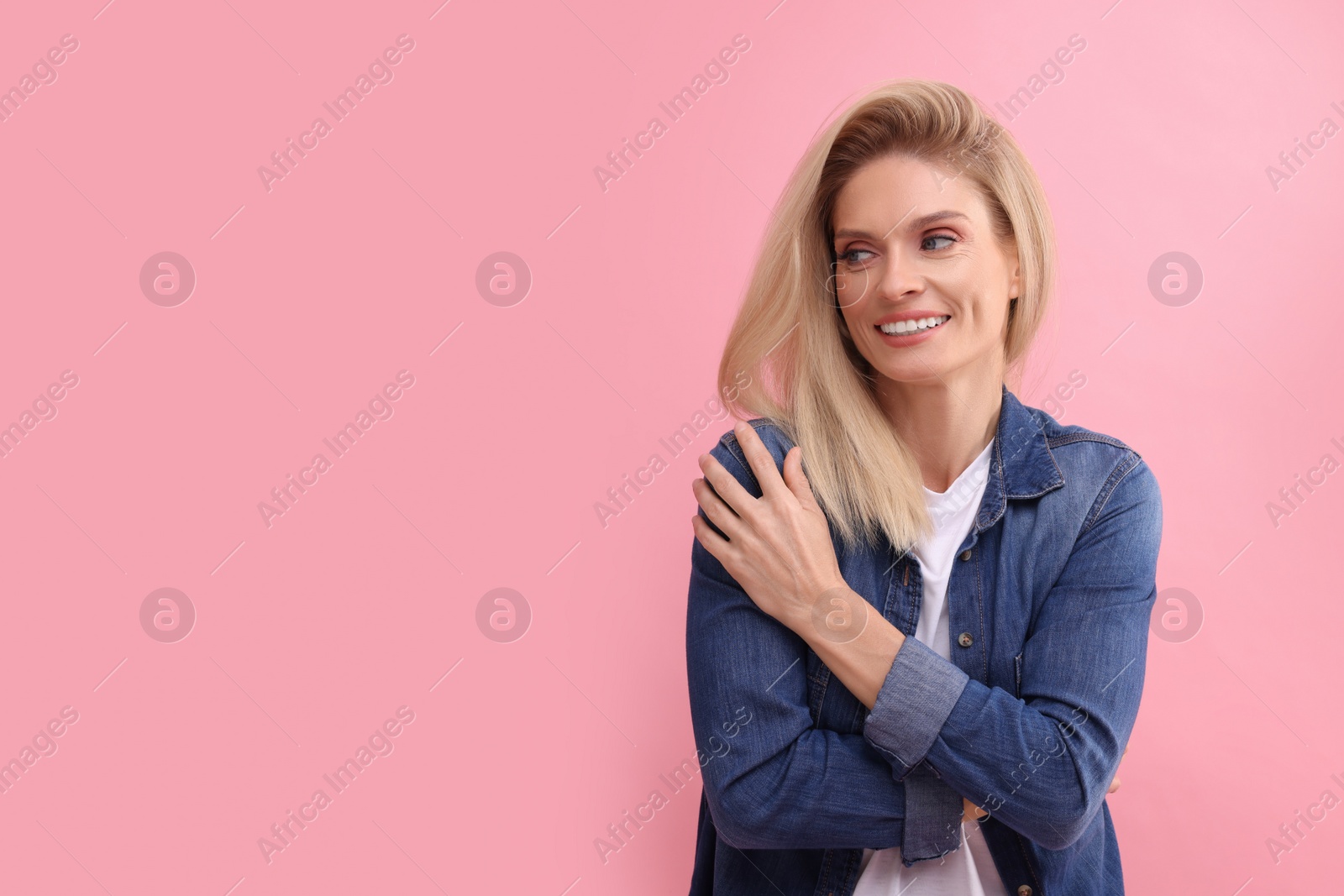 Photo of Portrait of smiling middle aged woman with blonde hair on pink background. Space for text