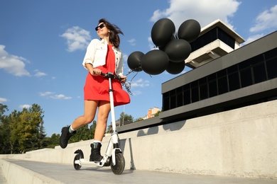 Young woman with black air balloons riding kick scooter along city street