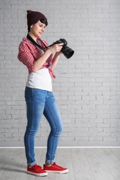 Photo of Young female photographer with camera near brick wall