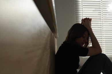 Photo of Sad young woman sitting indoors, space for text