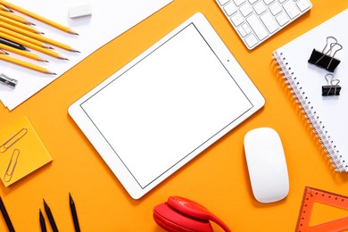 Modern tablet, keyboard and stationery on orange background, flat lay. Space for text