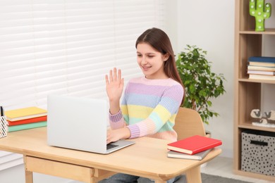 Cute girl using laptop at desk in room. Home workplace