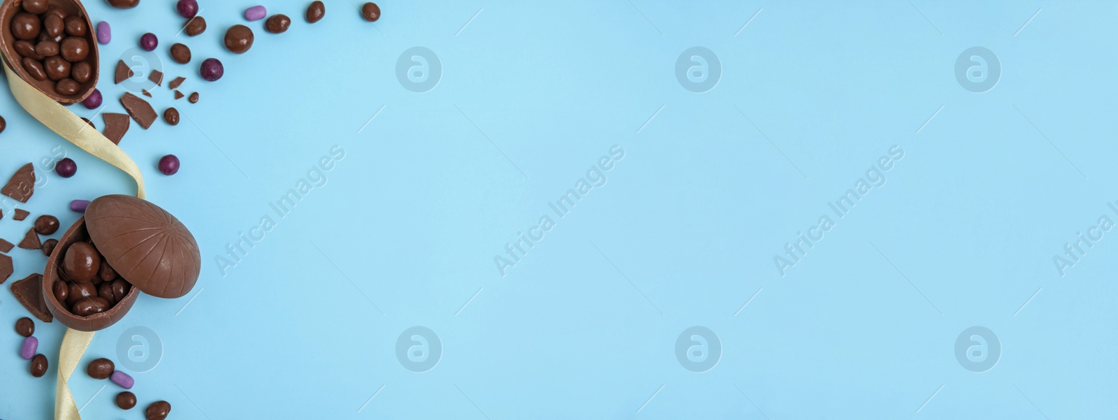 Image of Delicious chocolate eggs on light blue background, flat lay with space for text. Banner design