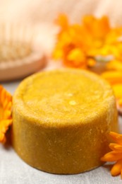 Photo of Yellow solid shampoo bar and flowers on light table, closeup. Hair care