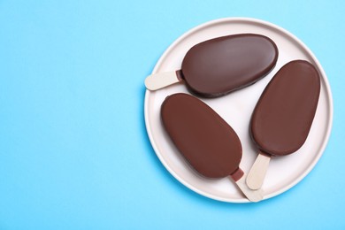 Plate with glazed ice cream bars on light blue background, top view. Space for text