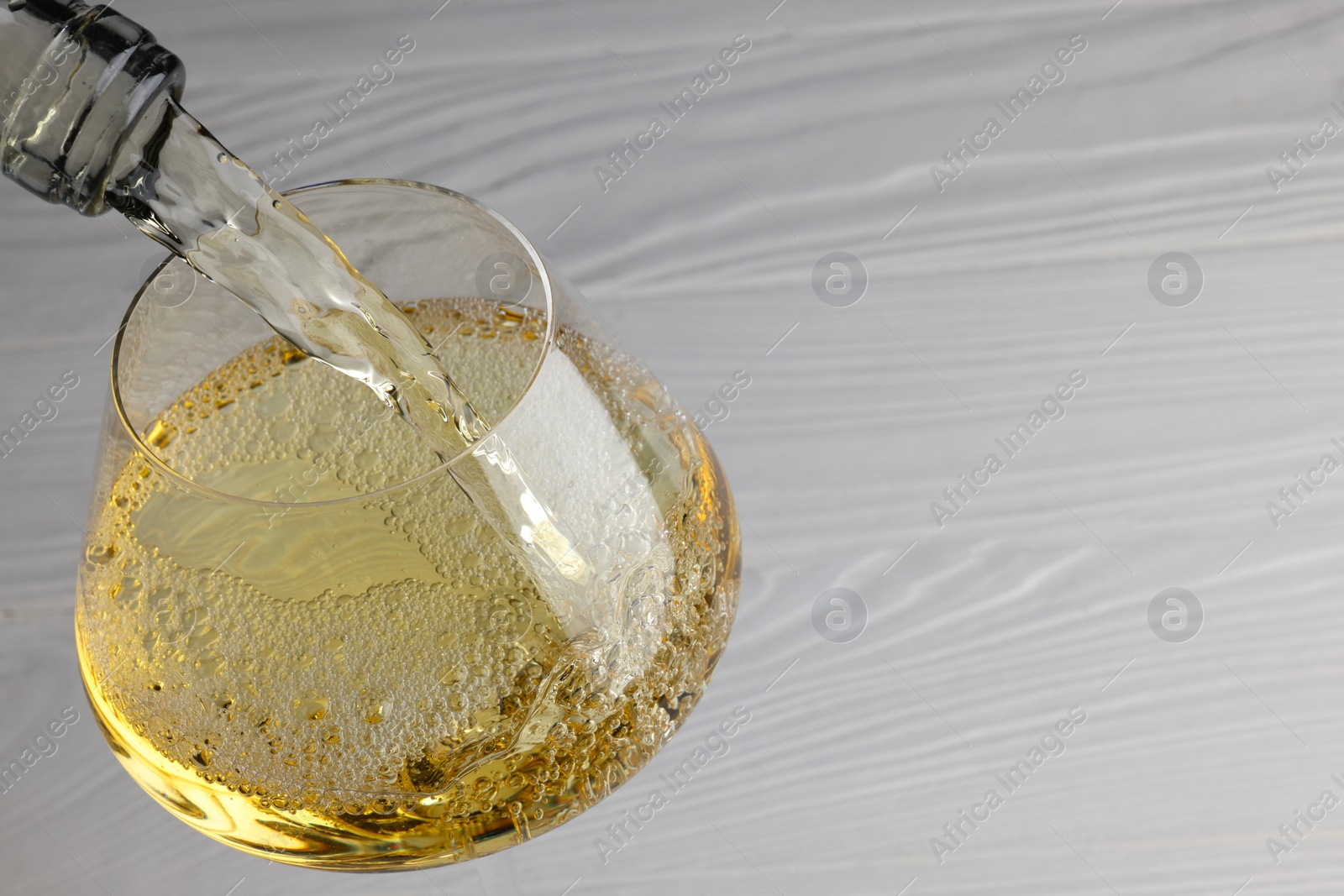 Photo of Pouring tasty aromatic wine in glass at white wooden table, closeup. Space for text