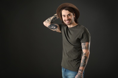 Photo of Young man with tattoos on arms against black background. Space for text