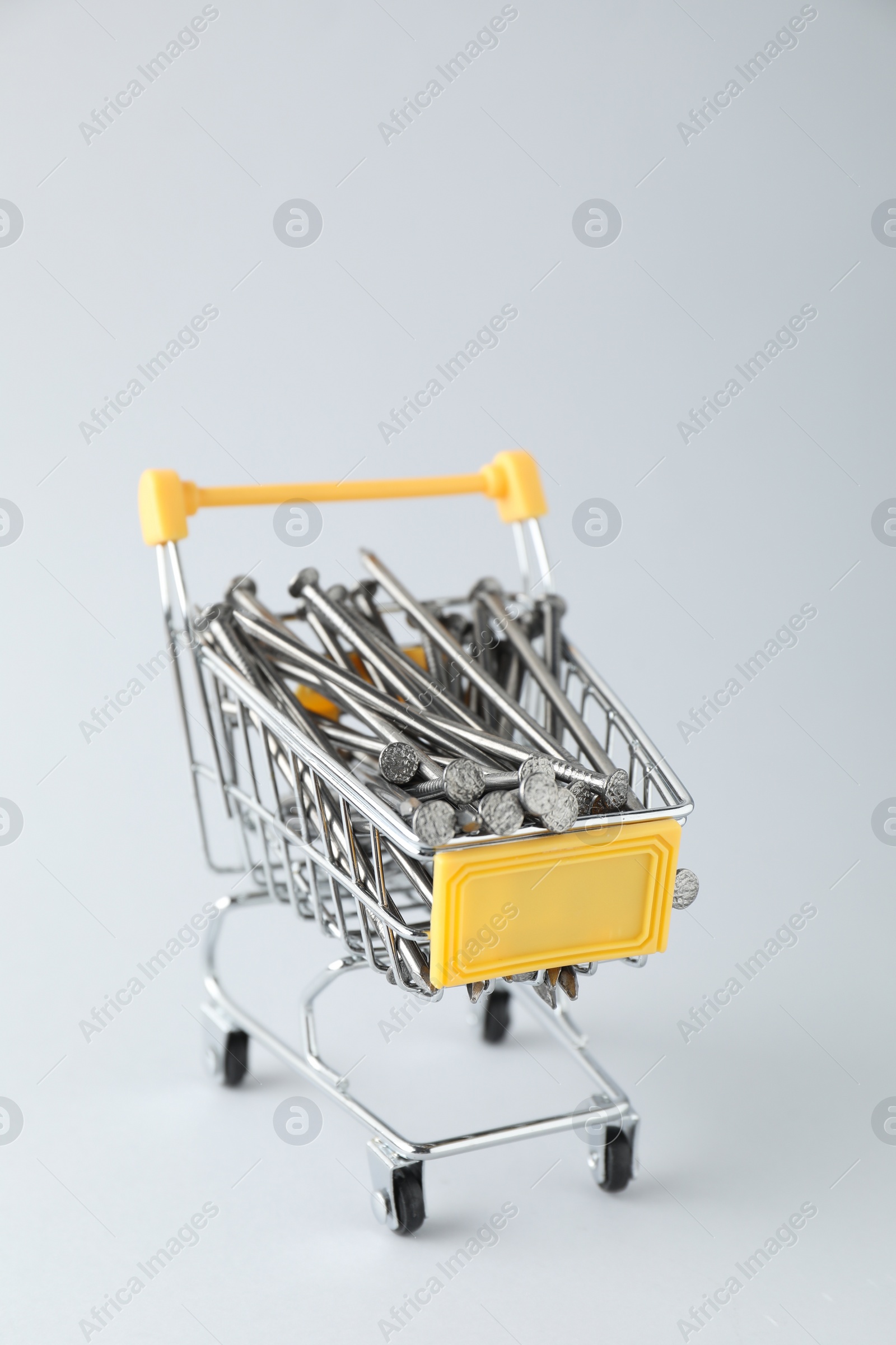 Photo of Metal nails in shopping cart on light grey background, closeup