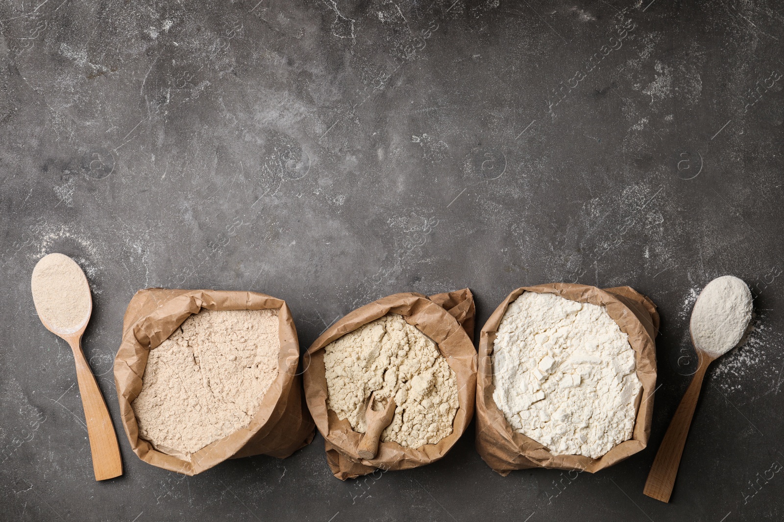 Photo of Paper bags with different types of flour on gray background