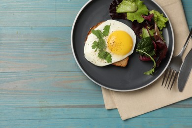 Photo of Delicious breakfast with fried egg and salad served on light blue wooden table, top view. Space for text