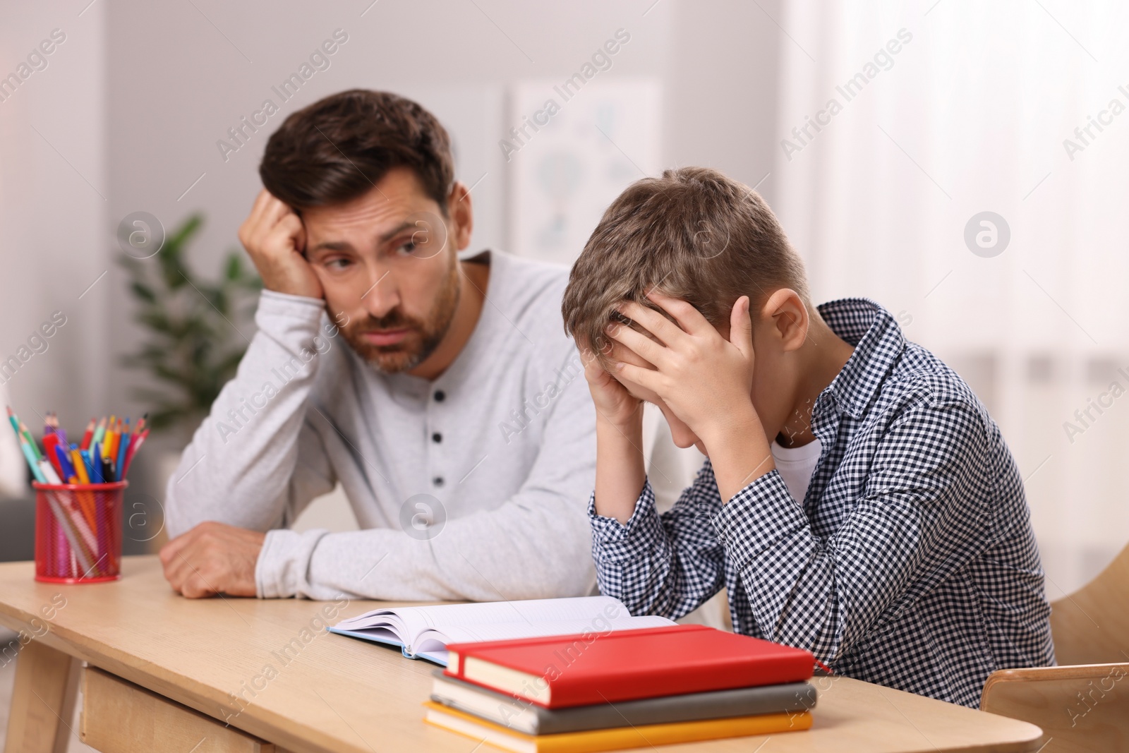 Photo of Dyslexia problem. Bored father helping son with homework at table in room, selective focus