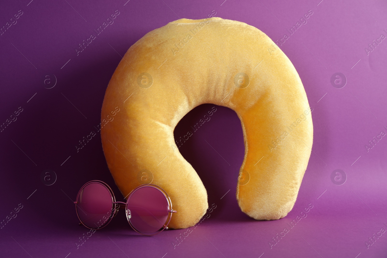 Photo of Yellow travel pillow and sunglasses on violet background