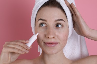 Young woman with acne problem applying cosmetic product onto her skin on pink background