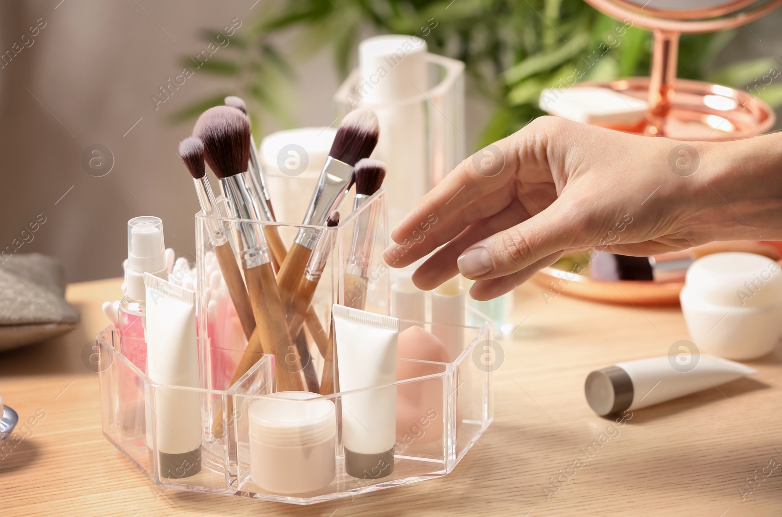 Photo of Woman taking cosmetic products from holder on dressing table, closeup