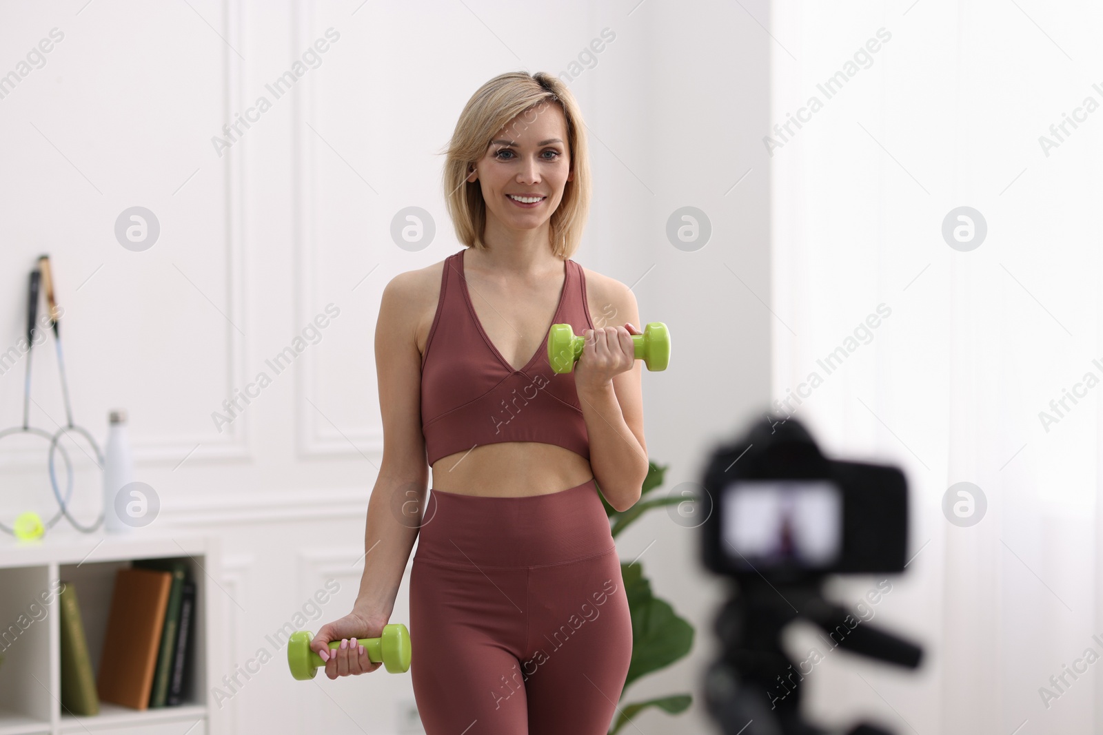 Photo of Smiling sports blogger working out with dumbbells while recording fitness lesson at home