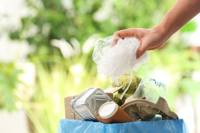 Man putting plastic bag into trash bin on blurred background, closeup with space for text. Recycling problem